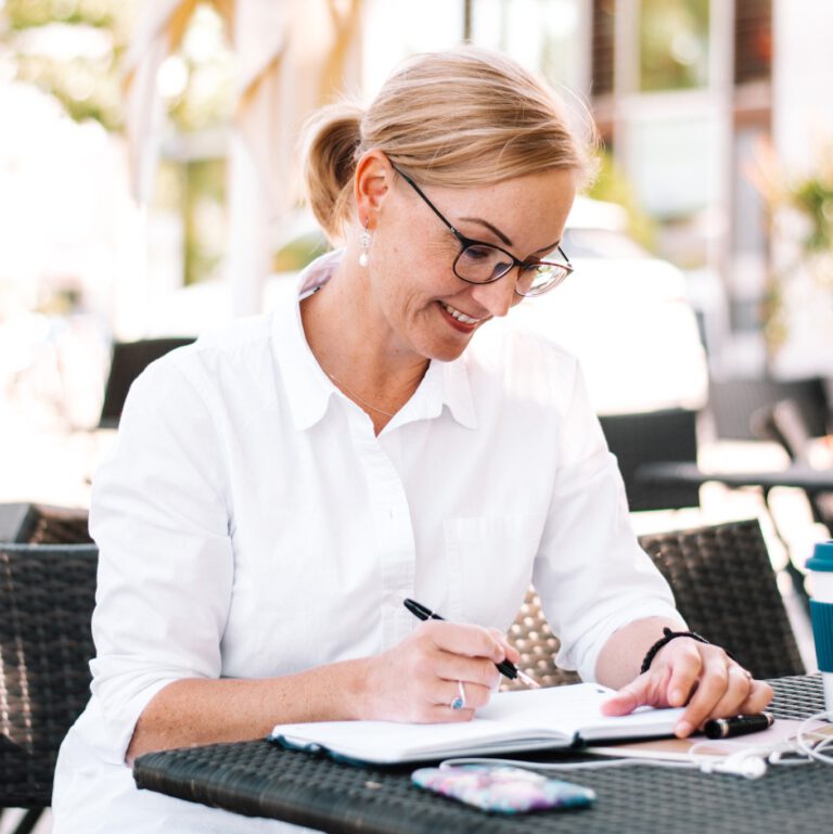 Anna sitting at table outside writing