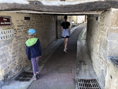 girls walking under low house down a road in france