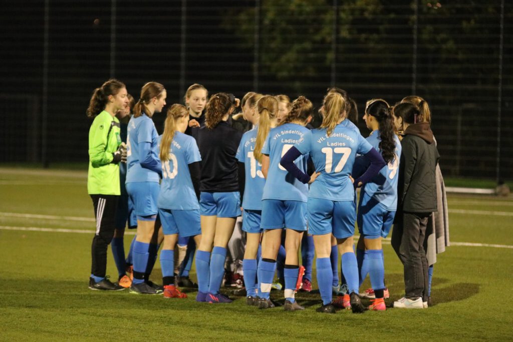 group of teenage girls in a huddle on a soccer field at night