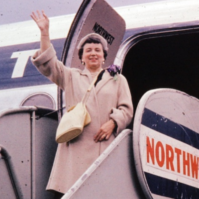 photo around 1965 of woman in hat waving as she boards a Northwest airlines flight
